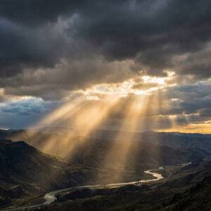 Sunbeams cutting through dark storm clouds over a mountainous landscape, illustrating the path of hope and light through the darkness of depression.