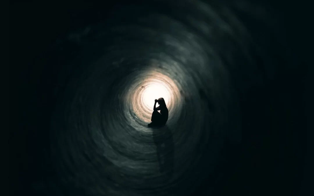 person sitting in dark tunnel with light at the end